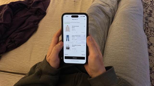 hands scrolling through an online shopping app on phone with items in cart visible from above angle